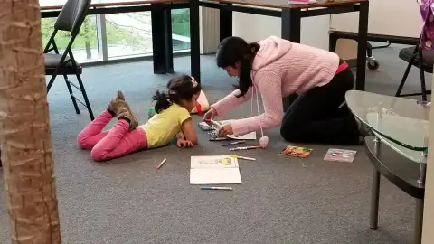 Parent and child coloring together on the floor with art supplies