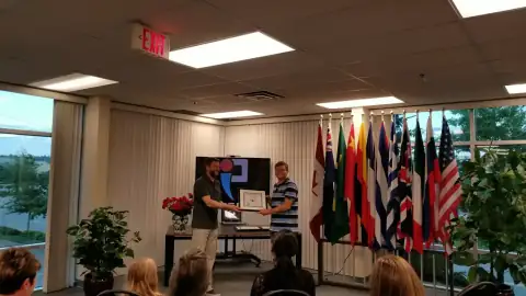 START Canada instructor presenting a framed certificate to a graduate in front of international flags