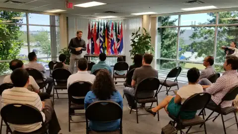 Speaker addressing an audience seated in front of a row of national flags