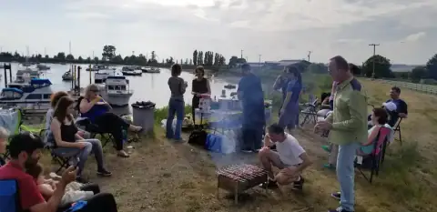 Group gathered by a riverside barbecue with boats in the background